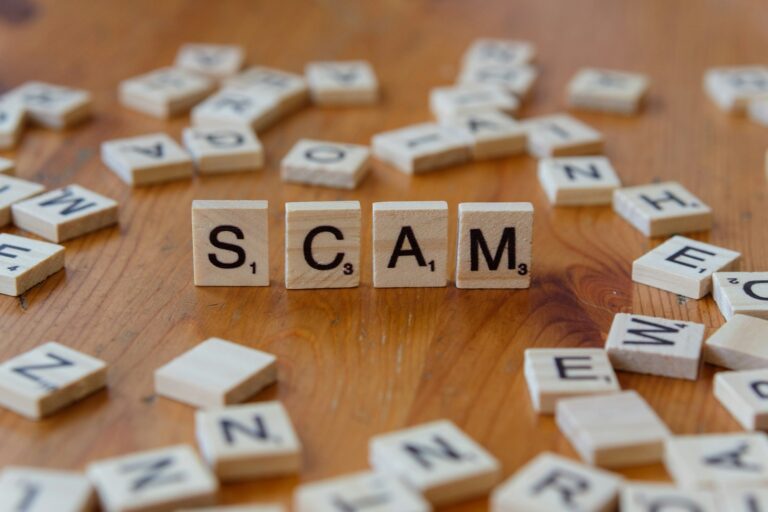 Kata SCAM tersusun dari huruf kayu di atas meja, menggambarkan ciri investasi bodong yang harus diwaspadai